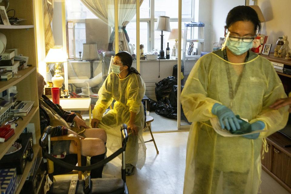Two women in PPE and an elderly man sitting in a chair