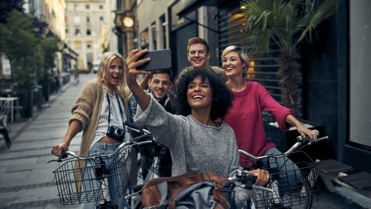 5 friends on bicycles with metal baskets in a city pedestrian zone taking selfie