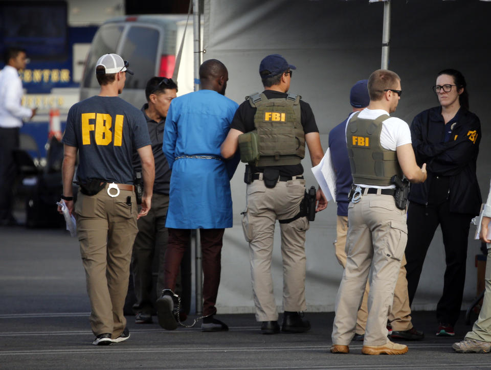 Federal agents hold a detainee, second from left, at a downtown Los Angeles parking lot after predawn raids that saw dozens of people arrested in the L.A. area Thursday, Aug. 22, 2019. U.S. authorities have unsealed a 252-count federal grand jury indictment charging 80 people with participating in a conspiracy to steal millions of dollars through a range of fraud schemes and laundering the funds through a Los Angeles-based network. The U.S. Attorney's Office says Thursday most of the defendants are Nigerian nationals. (AP Photo/Reed Saxon)