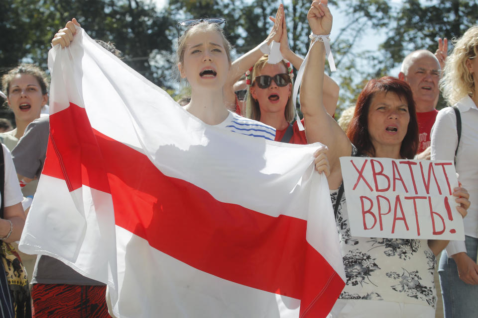 People hold an old Belarusian national flag, left, and a banner reading "Stop lying!" during a rally near the Belarus Television headquarters in Minsk, Belarus, Monday, Aug. 17, 2020. Thousands of factory workers are taking to the streets of Minsk demanding the resignation of authoritarian President Alexander Lukashenko, in the ninth straight day of protests against an election that extended his long rule over the country. (AP Photo/Dmitri Lovetsky)