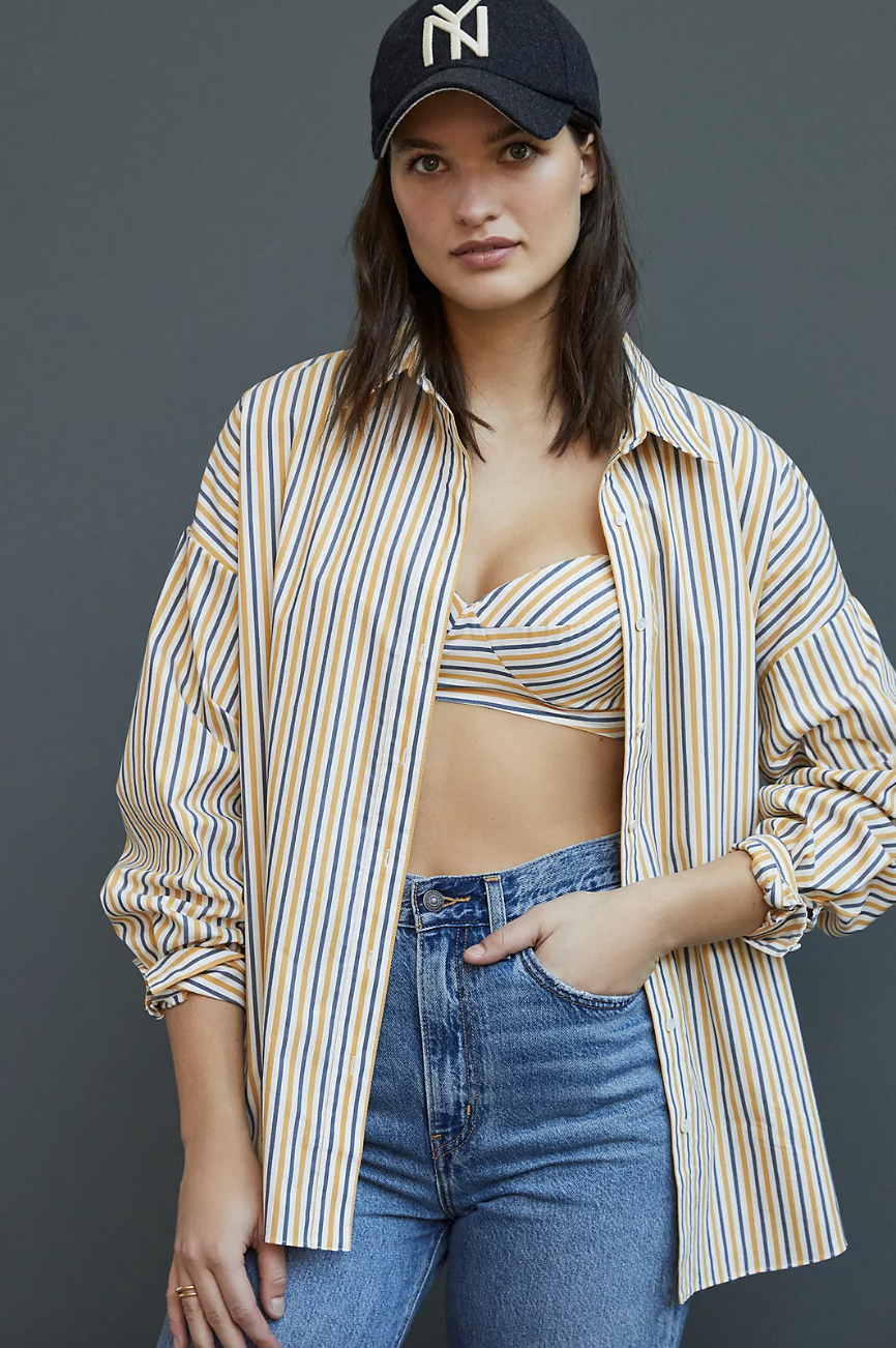 model in baseball cap, blue jeans, and striped bra with matching Favorite Daughter Long-Sleeved Striped Button-Down (Photo via Anthropologie)