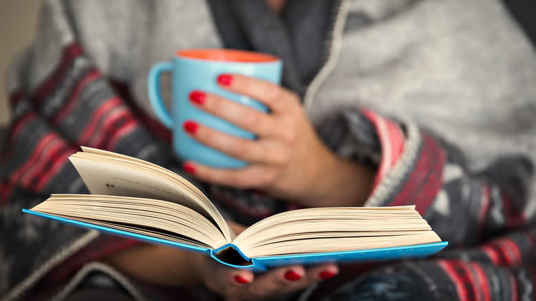 woman reading a book while holding a mug of hot cocoa