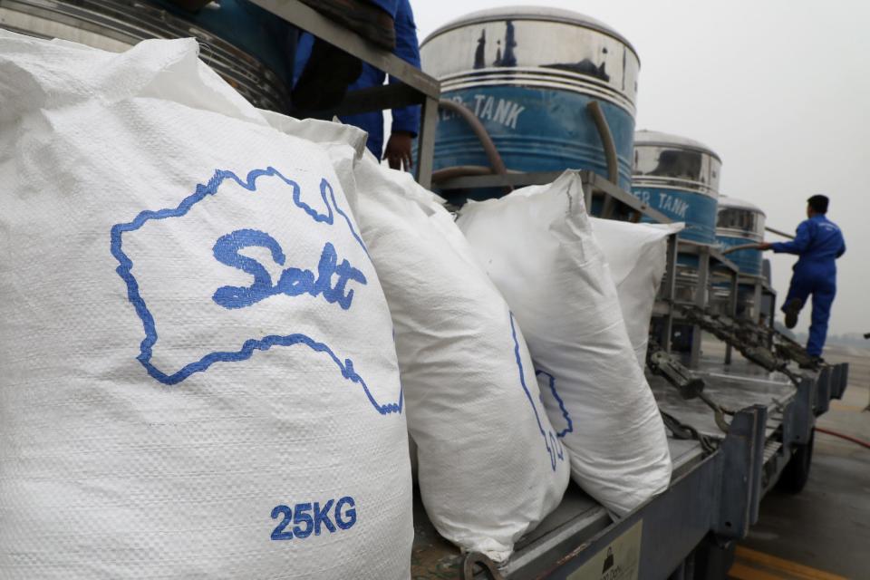 white bags reading "salt 25kg" lines up on a long metal truck bed with blue and silver tanks on it