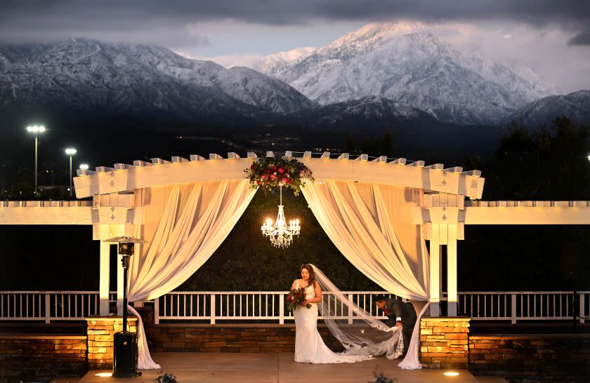 Upland, CA - February 26: Edgar Maria Marquez adjusts his wife Maria's wedding dress for their bridal photos at the Mountain Meadows golf course as clouds hang over the San Gabriel mountains on Sunday, Feb. 26, 2023 in Upland, CA. A storm system for the ages passed through Southern California on Saturday, dumping piles of snow in lower-elevation communities, closing key roads and leaving residents used to the region's dry, warm climate with a rare sense of icy wonder.(Wally Skalij / Los Angeles Times)