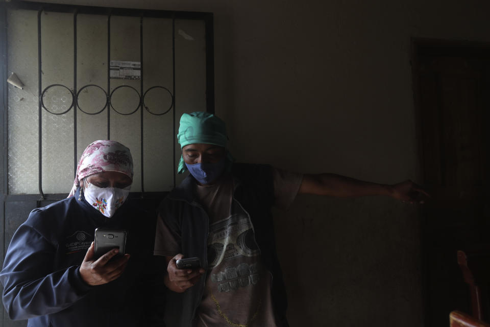 Con mascarilla para frenar la propagación del nuevo coronavirus, Perla Iguamba, directora de la escuela municipal de Cayambe, utiliza su celular para ayudar a Tobías Quinotoa, padre de tres alumnos del centro, para que puedan acceder a las clases virtuales desde su casa, en La Josefina, Ecuador, el 3 de septiembre de 2020. Los niños habían intentado conectarse con el servicio de internet de su casa, pero un apagón en el pueblo obligó a Iguamba a echarles una mano con su propio celular. (AP Foto/Dolores Ochoa)