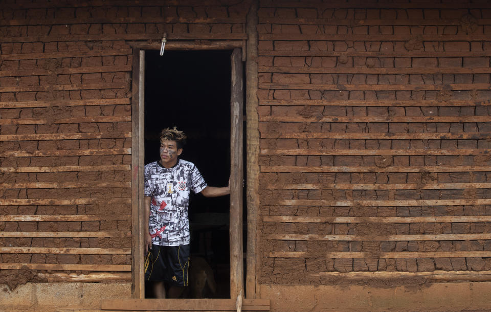 A Guarani Mbya youth peers from his traditionally built home on the indigenous community's land in Sao Paulo, Brazil, Friday, Jan. 31, 2020. Members of the tribe, living in the smallest demarcated indigenous land of Brazil, were surprised by workers with chainsaws who were making way for a five-building apartment complex in a nearby forested area. They say they weren’t consulted, as the law states, but the company has permits to build. The tension between a builder with projects in nine Brazilian states and a 40-family indigenous community is a microcosm of what’s playing out elsewhere in the country. (AP Photo/Andre Penner)