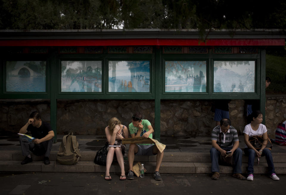 In this Wednesday, Aug. 28, 2013 photo, foreign and local tourists look at maps while sitting near a billboard showing scenes of the Summer Palace, a popular tourist destination in Beijing. China's new tourism slogan "Beautiful China" has been criticized by industry experts who say it illustrates a marketing problem that has led to a weakness in growth in foreign visitors over the past few years. (AP Photo/Andy Wong)