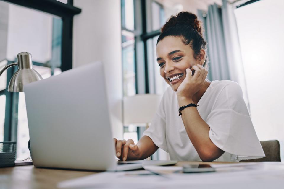 An investor smiles while looking at a laptop in an office.