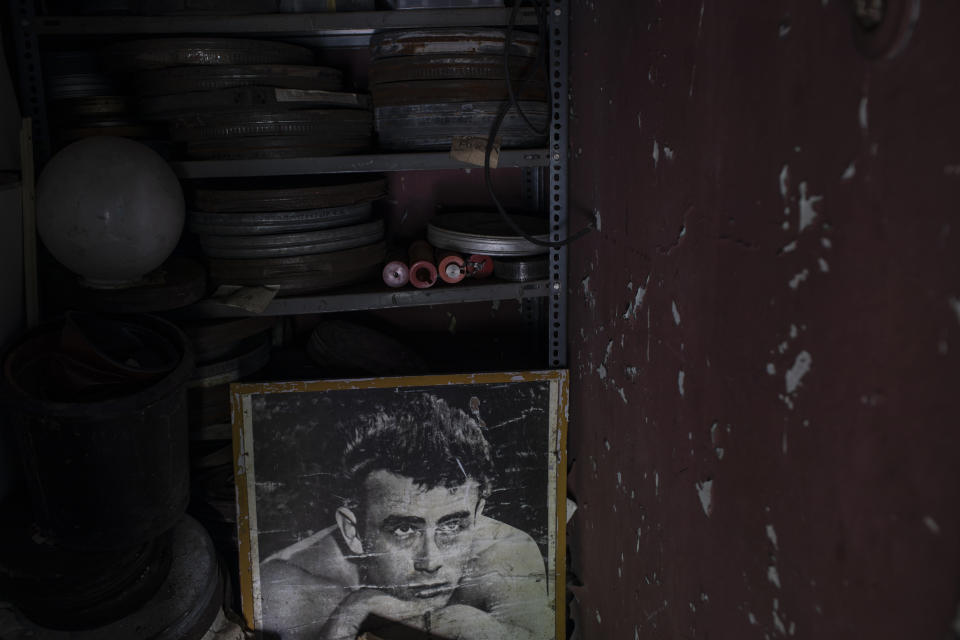 In this Friday May 29, 2020 photo a picture depicting American actor James Dean, who died in a 1955 car crash aged 24, stands beneath film reels at the Zephyros open-air cinema that specializes in films from past decades in the Petralona district in central Athens. (AP Photo/Petros Giannakouris)