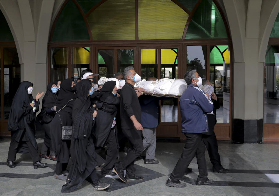 Mourners carry the body of a person who died from COVID-19, at the Behesht-e-Zahra cemetery on the outskirts of the Iranian capital, Tehran, Iran, Sunday, Nov. 1, 2020. The cemetery is struggling to keep up with the coronavirus pandemic ravaging Iran, with double the usual number of bodies arriving each day and grave diggers excavating thousands of new plots. (AP Photo/Ebrahim Noroozi)