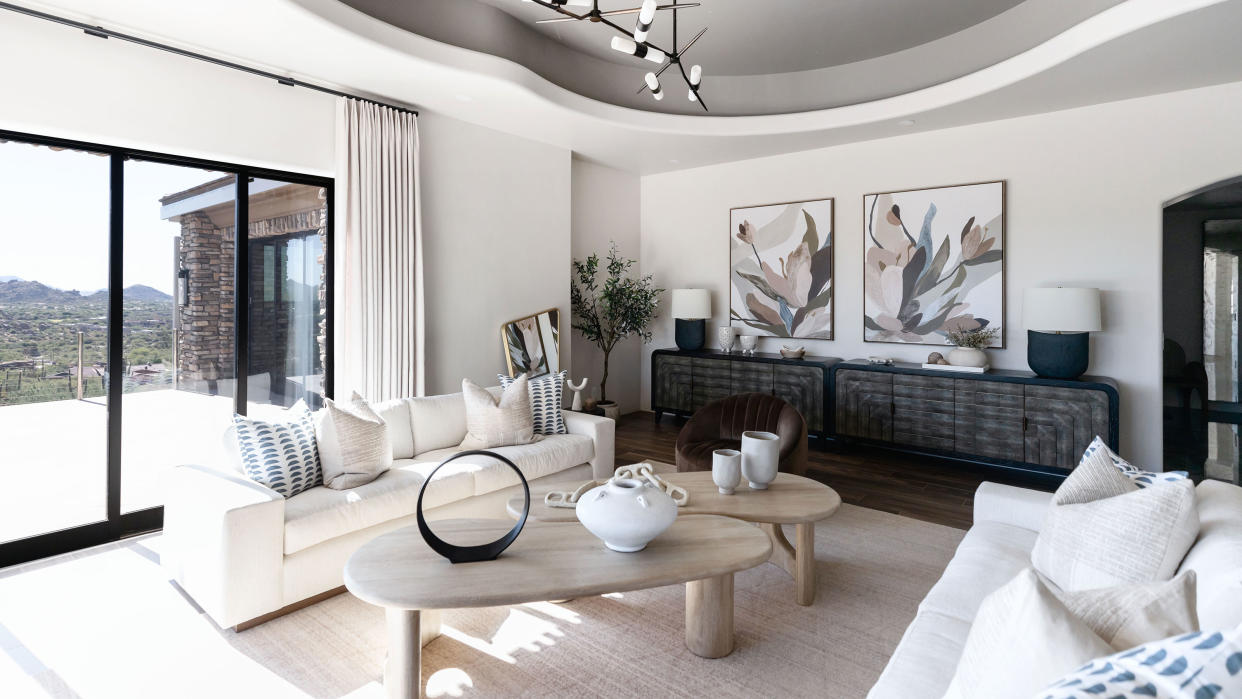  Minimal neutral living room with art on walls, circular coffee tables, accent pendant light, and cream couches. 