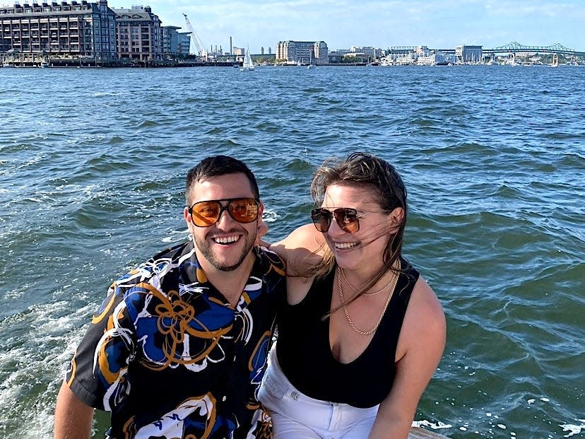 Meredith Wilshere and her boyfriend smiling and wearing sunglasses on a boat with water and a blue sky behind them.