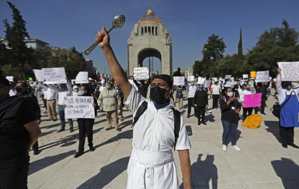 A worker with a metal cooking implement joins fellow restaurant employees in a protest against the COVID-19 "red alert” shutdown that suspended restaurants’ limited seating and returned to takeout and delivery only, in Mexico City, Thursday, Feb. 4, 2021. Although there has been an easing of restrictions allowing eateries to serve diners in socially distanced spaces, many restaurants do not have the expanse or outdoor patios to socially distance their diners. (AP Photo/Eduardo Verdugo)