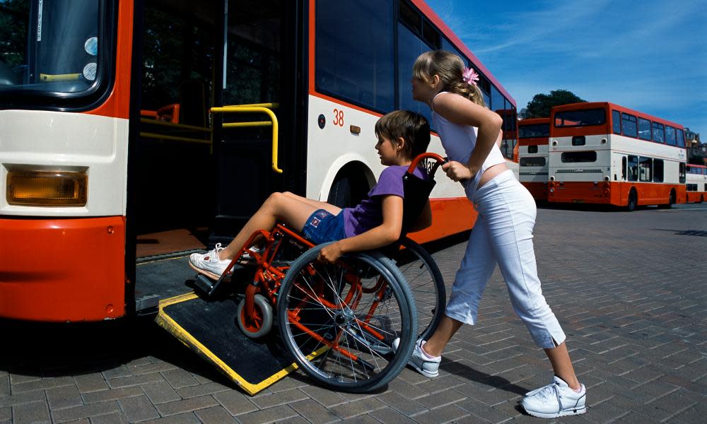 A boy in a wheelchair is helped onto a bus