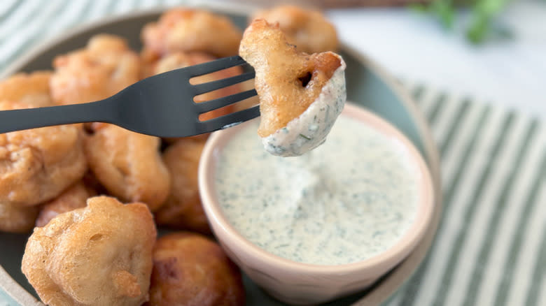 fork dipping fried mushrooms with ranch dressing