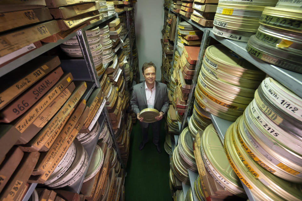 In this Wednesday, June 17, 2020 photo Gunnar Dedio, German film producer and managing director of PROGRESS Film GmbH poses for a photo between rolls of film in the archive of PROGRESS Film, in Leipzig, Germany. A new project is underway to digitize thousands of East German newsreels, documentaries and feature films 30 years after Germany’s reunification. The movies that are being scanned, transcribed and posted online provide a look inside a country that no longer exists but was a critical part of the Cold War. (AP Photo/Jens Meyer)