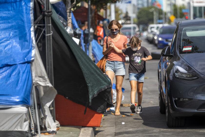 LOS ANGELES, CA - AUGUST 30: After school, Michelle Baron, walks with her daughter Penelope Baron past a homeless encampment near Larchmont Charter School - Selma located in the Hollywood neighborhood on Monday, Aug. 30, 2021 in Los Angeles, CA. The street becomes congested with vehicles as families arrive to pick up their children. Because the sidewalk is blocked with tents families and students end up walking in the street past the tents in between cars. (Francine Orr / Los Angeles Times)