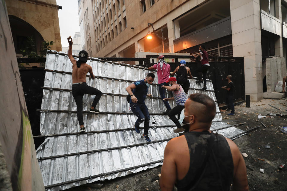 People climb a police barrier during anti-government protest following Tuesday's massive explosion which devastated Beirut, Lebanon, Sunday, Aug. 9. 2020. (AP Photo/Hassan Ammar)