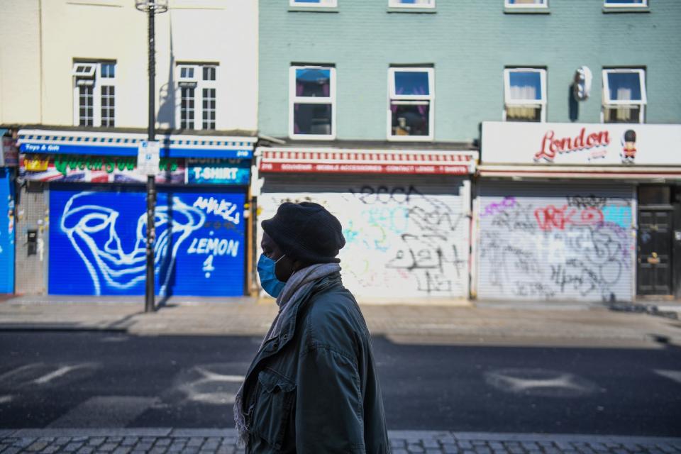 A woman wearing a mask walks down an empty Camden High Street during coronavirus lockdown (PA)