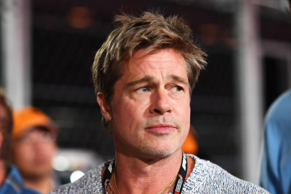 Brad Pitt wearing a casual knit sweater and a lanyard, looking slightly to the side while attending an event