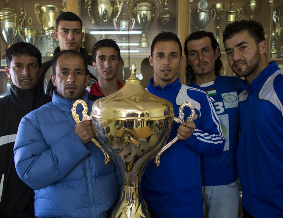 In this Tuesday, Feb. 11, 2014 photo, Abu Hammad family members pose with the Yasser Arafat Cup at their club's trophy room in the West Bank village of Wadi al-Nees. Palestinian farmer Yousef Abu Hammad sired enough boys for a soccer team and the current roster of the Wadi al-Nees team includes six of Abu Hammad's sons, three grandsons and five other close relatives. Wadi al-Nees heads the West Bank's 12-team “premier league,'' consistently defeating richer clubs and believe their strong family bonds are a secret to their success. (AP Photo/Dusan Vranic)