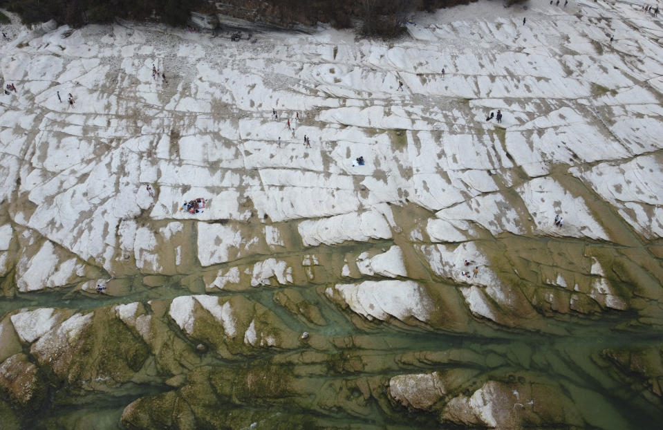 People sunbath on the peninsula of Sirmione, on Garda lake, Italy, Friday, Aug. 12, 2022. Lake Garda water level has dropped critically following severe drought resulting in rocks to emerge around the Sirmione Peninsula. (AP Photo/Antonio Calanni)