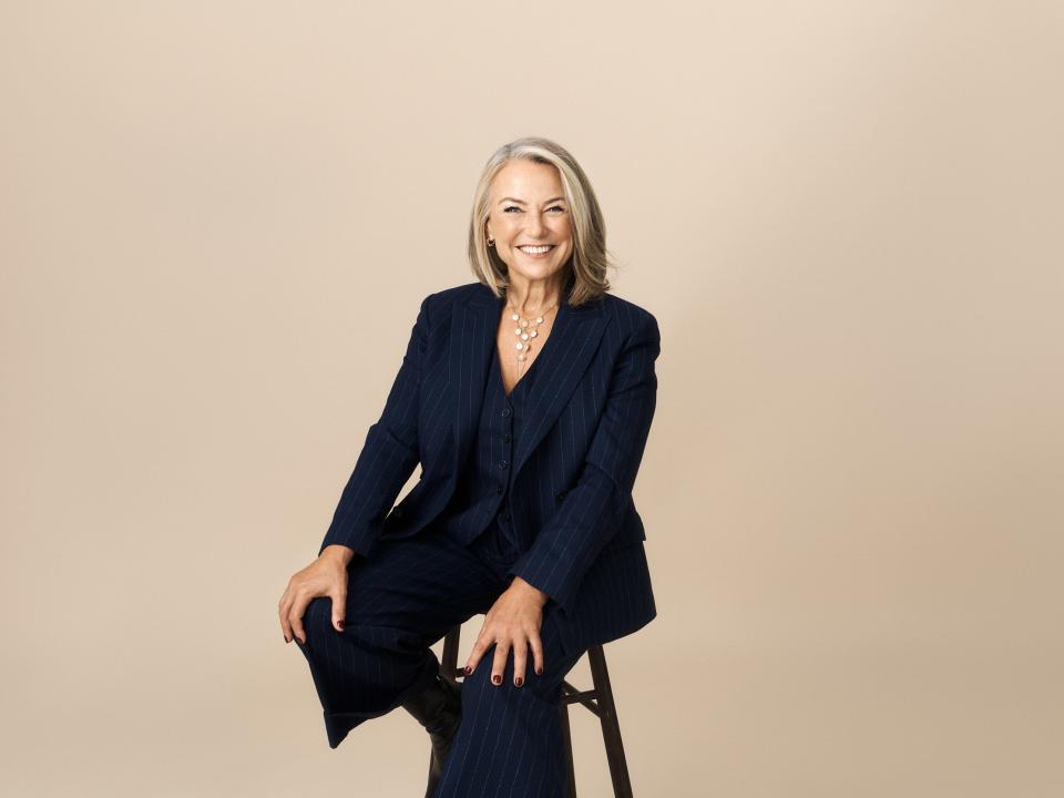 Esther Perel sitting on a black stool in front of a beige background