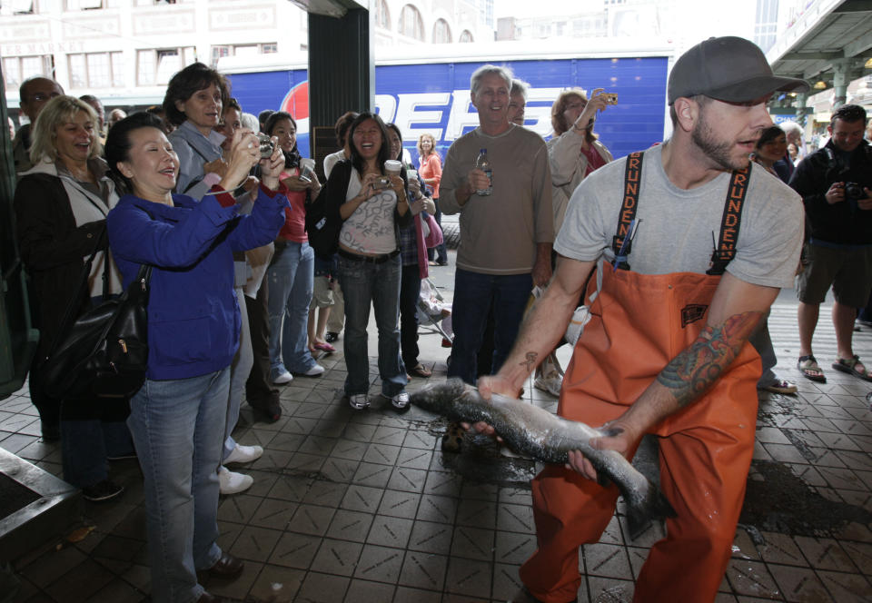 FILE - This July 11, 2009 file photo shows Justin Hall throwing a salmon to a co-worker behind the counter at Pike Place Fish, at Pike Place Market in Seattle. The market and the fish throw are a favorite and free attraction for visitors to Seattle. (AP Photo/Ted S. Warren, file)