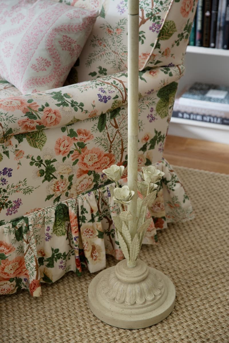 Close up on white standing lamp base with iron flowers, floral pattern couch with ruffle skirt