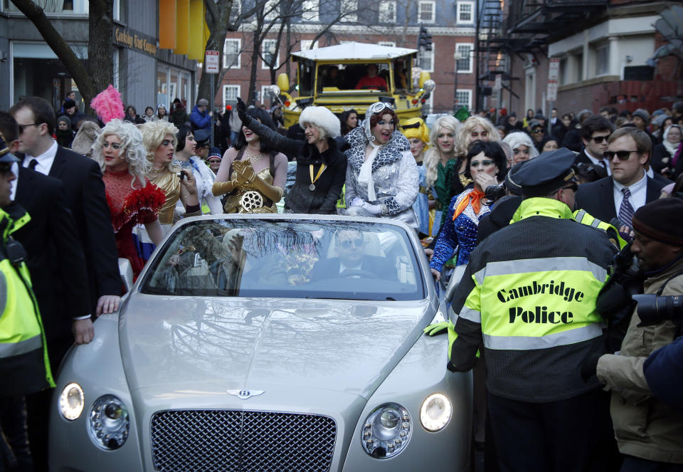 Actress Helen Mirren waves from a Bentley convertible, accompanied by drag actors Tony Oblen, left, and Ethan Hardy, right, while she is paraded through Harvard Square as woman of the year by Harvard University's Hasty Pudding Theatricals in Cambridge, Mass., Thursday, Jan. 30, 2014. (AP Photo)
