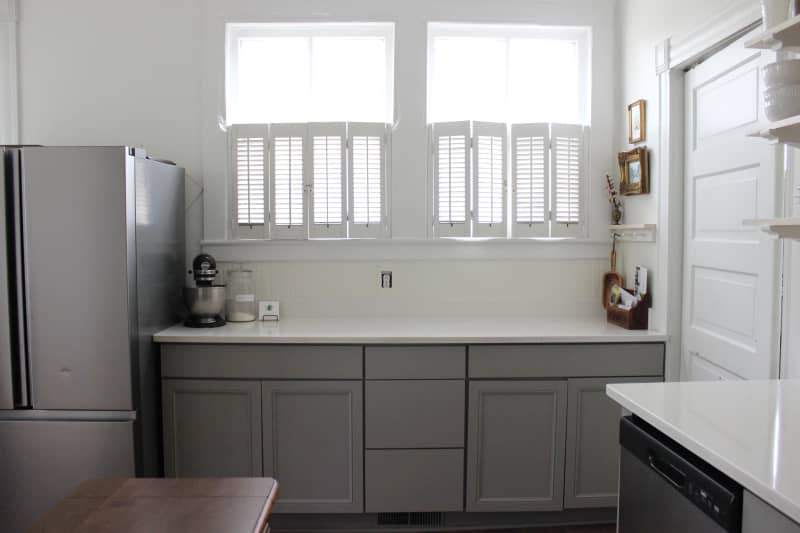 A bright kitchen with grey cabinetry and half-window shutters before the renovation.