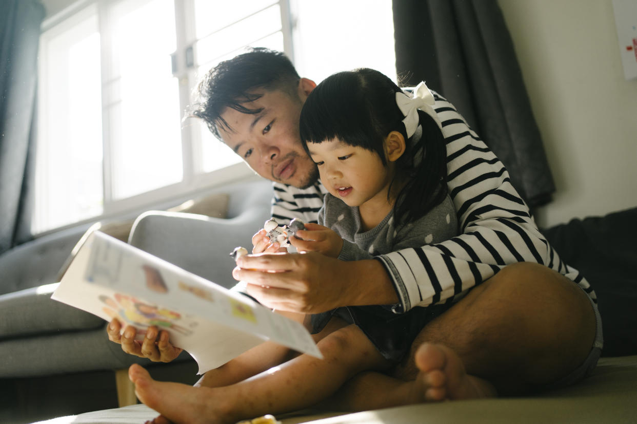 Father reading a book with daughter at home. (Photo: Getty)