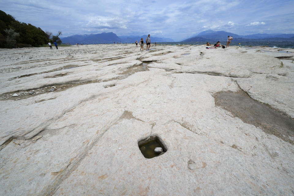 People walk on the peninsula of Sirmione, on Garda lake, Italy, Friday, Aug. 12, 2022. Lake Garda water level has dropped critically following severe drought resulting in rocks to emerge around the Sirmione Peninsula. (AP Photo/Antonio Calanni)