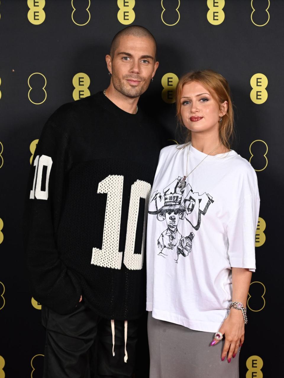 max george and maisie smith, a couple stand looking at the camera slightly smiling and wearing casual tshirts