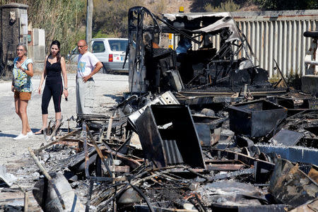 People stand near charred debris of vehicles that were destroyed by fire in a parking lot for camping cars in Bormes-les-Mimosas, in the Var department, France, July 26, 2017, after firefighters evacuated thousands of campers and local residents when a wildfire broke out on France's tourist-thronged Riviera coast overnight. REUTERS/Jean-Paul Pelissier