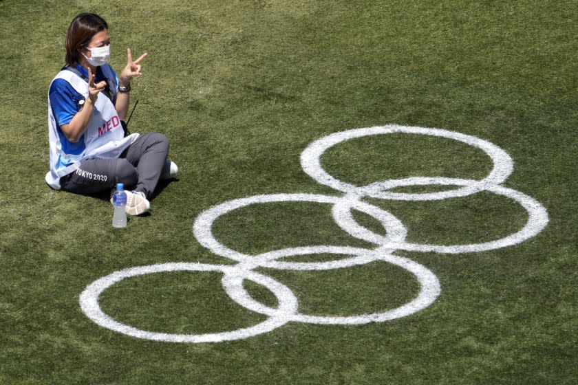 A worker poses for a photo with a set of Olympic rings before a softball practice for the 2020 Summer Olympics, Saturday, July 17, 2021, at Yokohama Baseball Stadium in Yokohama, Japan. (AP Photo/Charlie Riedel)