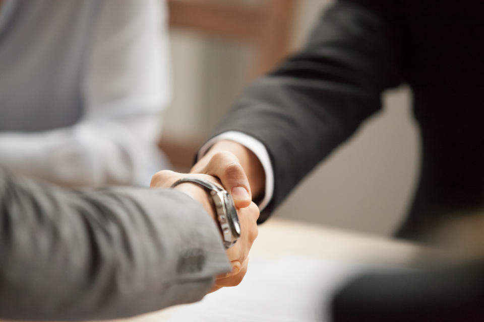 Guys in suits shaking hands across a table.