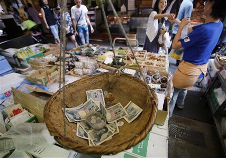 Coins and banknotes that are used for change are seen in a bamboo basket at a greengrocer in Tokyo in this August 22, 2013 file photo. Japan's top two financial ministers openly disagreed on whether a corporate tax cut was needed to cushion any pain from an increase in the sales tax, as the government upgraded its view of the economy on Friday for the seventh time this year. REUTERS/Toru Hanai