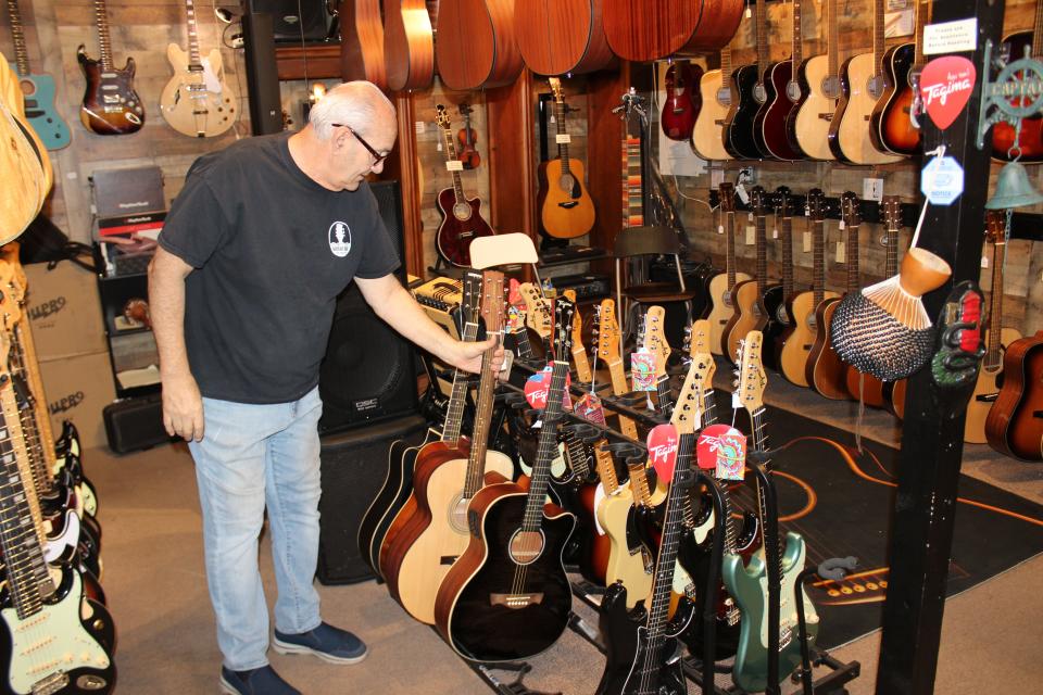 Dennis Del Prete, owner of Dunes Mercantile on Oak Island, checks his stock of guitars on July 28.