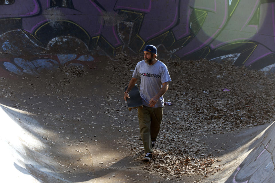 Skateboarder Dallas Oberholzer, 46, walks with his skateboard at at the Germiston Lake Skateboard Park, near Johannesburg, Saturday, July 3, 2021. The age-range of competitors in skateboarding's Olympic debut at the Tokyo Games is remarkably broad and Oberholzer will go wheel-to-wheel with skaters less than half his age. (AP Photo/Denis Farrell)