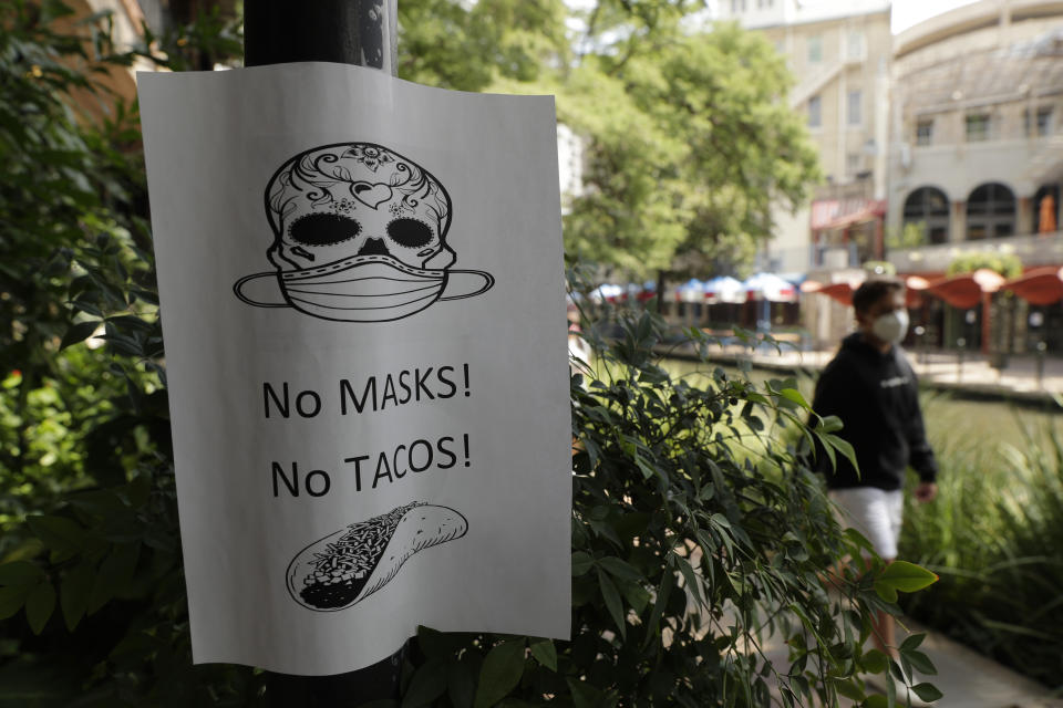 A man wearing a mask to protect against the spread of COVID-19 passes a sign requiring masks at a restaurant, Tuesday, July 7, 2020, in San Antonio. Texas Gov. Greg Abbott has declared masks or face coverings must be worn in public across most of the state as local officials across the state say their hospitals are becoming increasingly stretched and are in danger of becoming overrun as cases of the coronavirus surge. (AP Photo/Eric Gay)