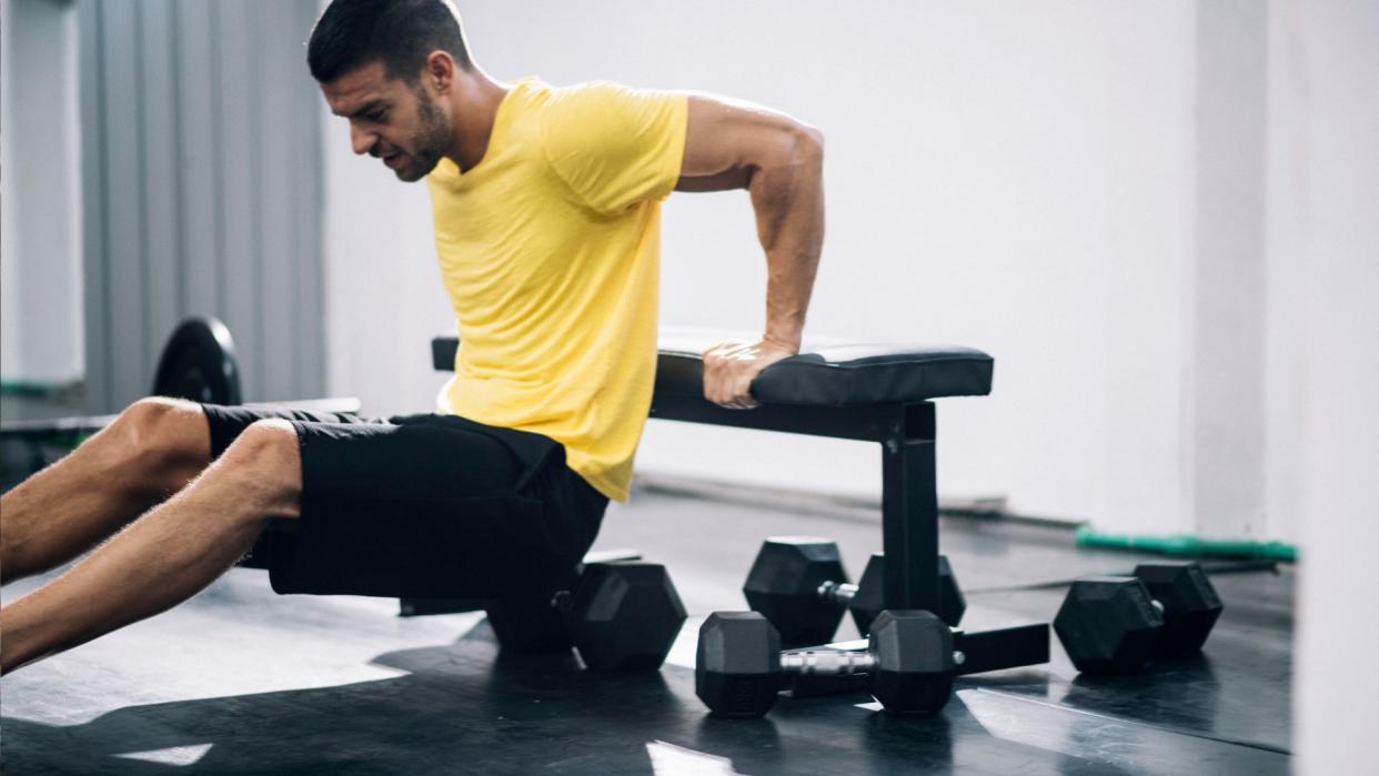  Man performing tricep dips on a weight bench. 