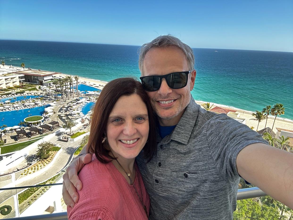 kari and her husband posing for a selfie on the balcony of an all inclusive resort on the ocean