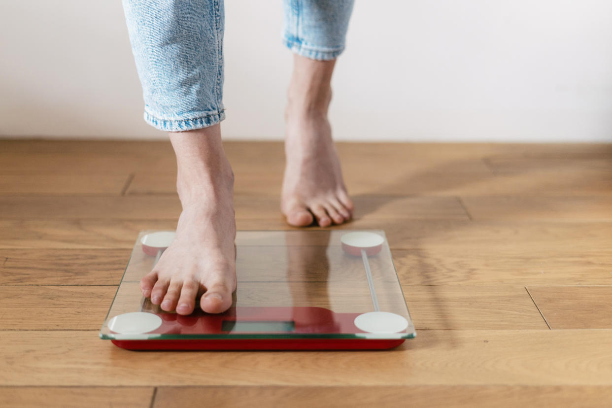 weight loss Cropped shot of young barefoot woman in casual blue jeans step on the floor scales to check her weight at home. Concept of bmi control and keeping the body in shape