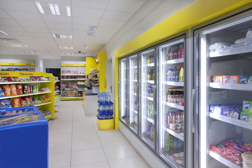 Interior of a convenience store with snacks and refrigerated items on display, aisle leading to the cashier