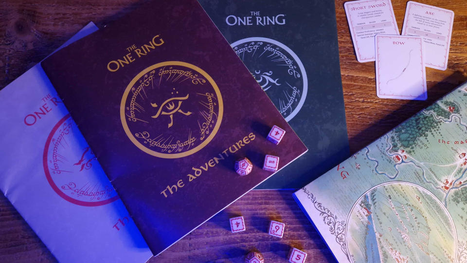 The One Ring Starter Set rulebooks, dice, cards, and map laid out on a wooden table