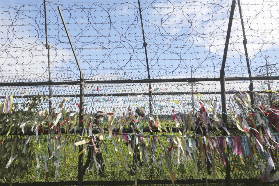 South Korean army soldiers wearing face masks to help protect against the spread of the new coronavirus pass by a wire fence decorated with ribbons written with messages wishing for the reunification of the two Koreas at the Imjingak Pavilion in Paju, near the border with North Korea, Sunday, July 26, 2020. North Korean leader Kim Jong Un placed the city of Kaesong near the border with South Korea under total lockdown after a person was found with suspected COVID-19 symptoms, saying he believes "the vicious virus" may have entered the country, state media reported Sunday. (AP Photo/Ahn Young-joon)