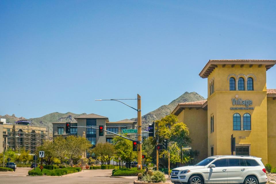 A complex with adobe buildings and lush greenery with mountains and clear, blue skies in the background