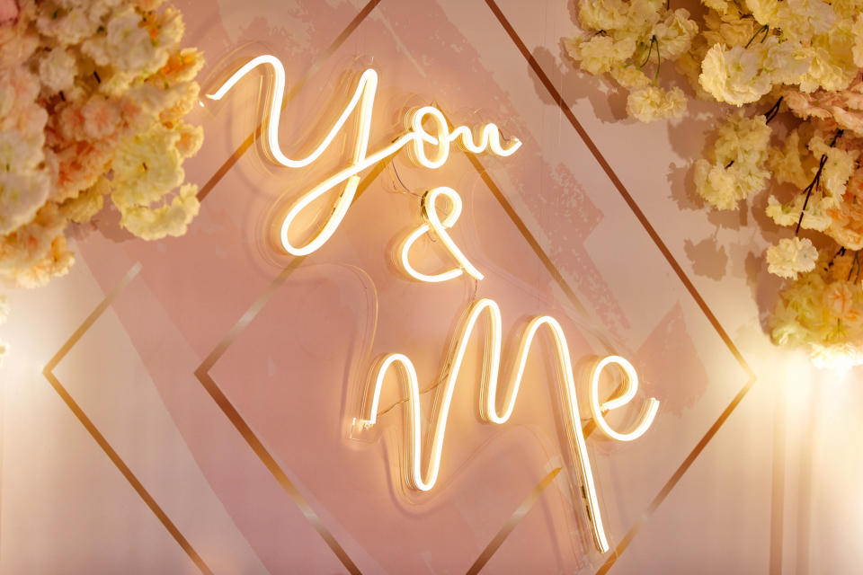 Neon sign reading "You & Me" surrounded by floral arrangements, suitable for wedding decor