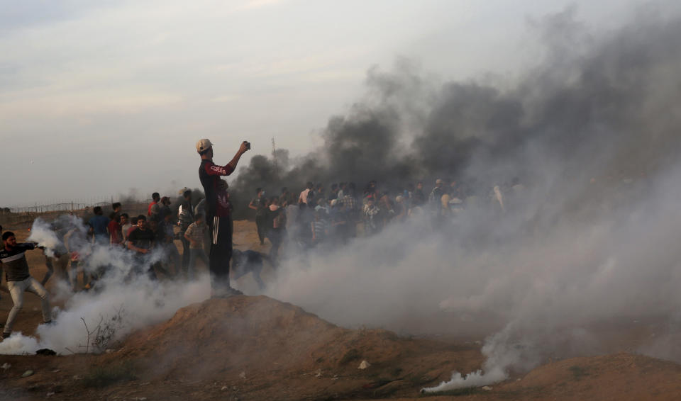 A protester takes photos while others run for cover from teargas fired by Israeli troops while others burn tires near the fence of the Gaza Strip border with Israel during a protest east of Khan Younis, southern Gaza Strip, Friday, Oct. 5, 2018. Israeli forces shot dead three Palestinians, including a 13-year-old boy, as thousands of people protested Friday along the fence dividing the Gaza Strip and Israel, Gaza's Health Ministry said. (AP Photo/Adel Hana)